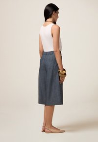 Falda de chambray azul con cintura alta, bolsillos frontales y diseño hasta la rodilla, combinada con una camiseta de tirantes blanca y zapatos slingback beige.