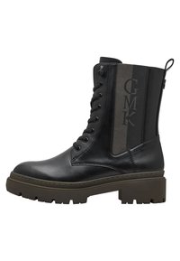 Bottine noire avec une finition en cuir brillant, devant à lacets et panneau élastique latéral arborant un logo. Semelle épaisse et robuste pour une bonne traction.