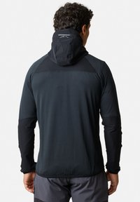 Zwarte sportjack met capuchon, voorzien van contrasterende stofpanelen, textuur op het lichaam en een klein logo op de achterkant van de capuchon.