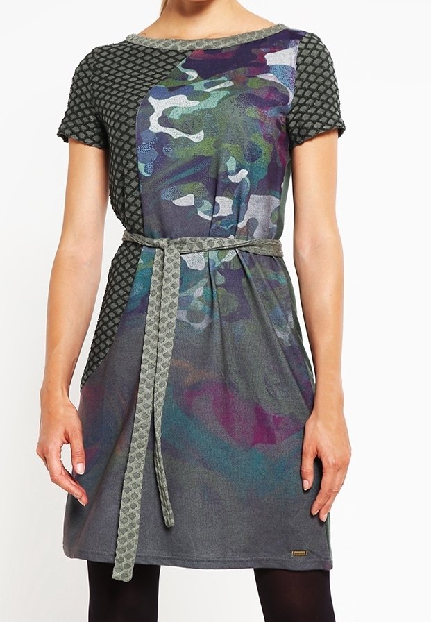 Femme portant une robe grise à manches courtes avec des motifs mélangés, un imprimé camouflage au centre, des manches géométriques et une ceinture tressée nouée à la taille.