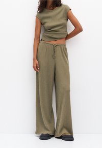 Ensemble deux pièces vert olive à côtes comprenant un haut ajusté à manches courtes et un pantalon à jambes larges avec une taille élastique et un cordon de serrage.