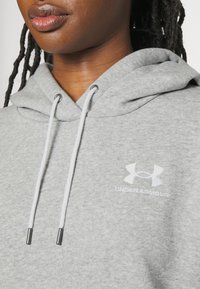 Felpa grigia Under Armour con cordini, caratterizzata da una texture morbida e un piccolo logo bianco sul petto.