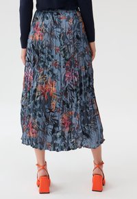 Gonna plissettata floreale in tessuto blu, con vivaci motivi floreali; abbinata a sandaletti arancioni con tacco a blocco.