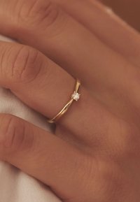 Gouden ring met een delicate band en een kleine, ronde diamantaccent. Glad afwerkingsoppervlak, dun profiel en een minimalistisch ontwerp.