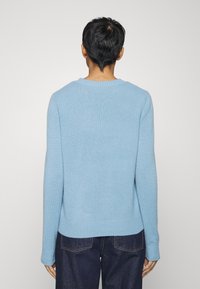 Pull en tricot bleu clair avec un col rond, des manches longues et des poignets et un ourlet côtelés. Le tissu semble doux et texturé.