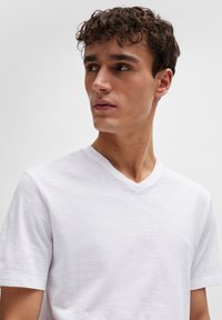 Valkoinen, lyhythihainen V-pääntie T-paita, joka on valmistettu kevyestä kankaasta; siinä on hienovarainen pintastruktuuri ja rento istuvuus.