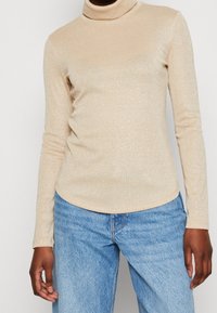 Beige coltrui gemaakt van een glanzende stof, met lange mouwen en een aansluitende pasvorm, gecombineerd met lichtblauwe denim jeans.