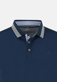 Marinblå polo med en kontrastfärgad krage, knäppning med två knappar och logotyp. Har ett mönstrat foder och texturerad tyg.