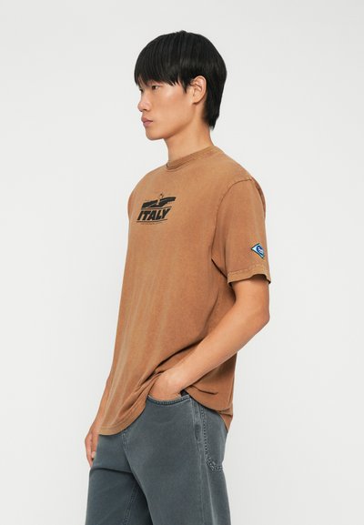 Brun bomull t-skjorte med rund hals, korte ermer og et grafisk trykk som sier "ITALY" på forsiden. Slim fit, avslappet stil.