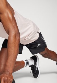 Ροζ αμάνικο μπλουζάκι, μαύρα σορτσάκια με πλαϊνές ρίγες, μαύρα αθλητικά παπούτσια και λευκές κάλτσες με μαύρες ρίγες, προβάλλοντας μυώδη χέρια και πόδια.