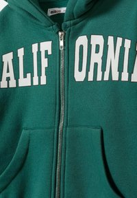 Sweat à fermeture éclair vert avec un grand texte blanc "CALIFORNIA". Fabriqué en tissu doux, il comporte une poche avant et des détails en zip argenté.