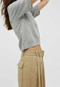 Szary sweter z krótkim rękawem zestawiony z beżowymi spodniami o podwyższonym stanie, które mają szeroki pasek, zakładki i boczne kieszenie. Gładka tekstura na całej powierzchni.