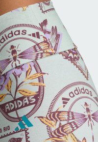 Adidas leggings világos mentazöld háttérrel, lila, sárga és sötétvörös virág- és rovargrafikákkal. Kék Adidas logót tartalmaz.
