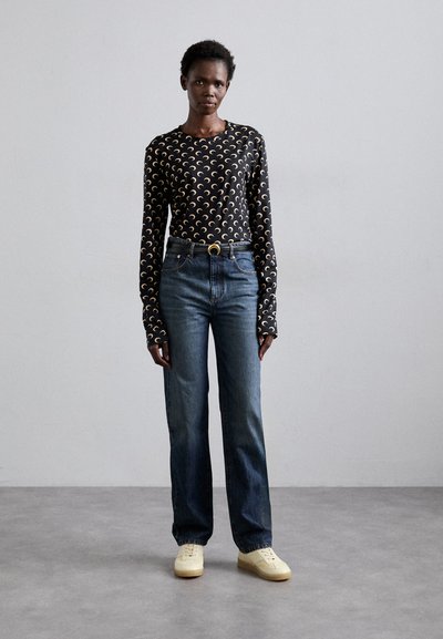 Camisola de manga longa preta com padrão de lua crescente dourada, combinada com jeans de perna reta azuis e ténis de cor clara. Design minimalista.