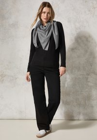 Maglione nero con zip frontale, abbinato a pantaloni neri. Una sciarpa grigia con un motivo maculato penzola attorno al collo. Sneakers bianche con accenti grigi.