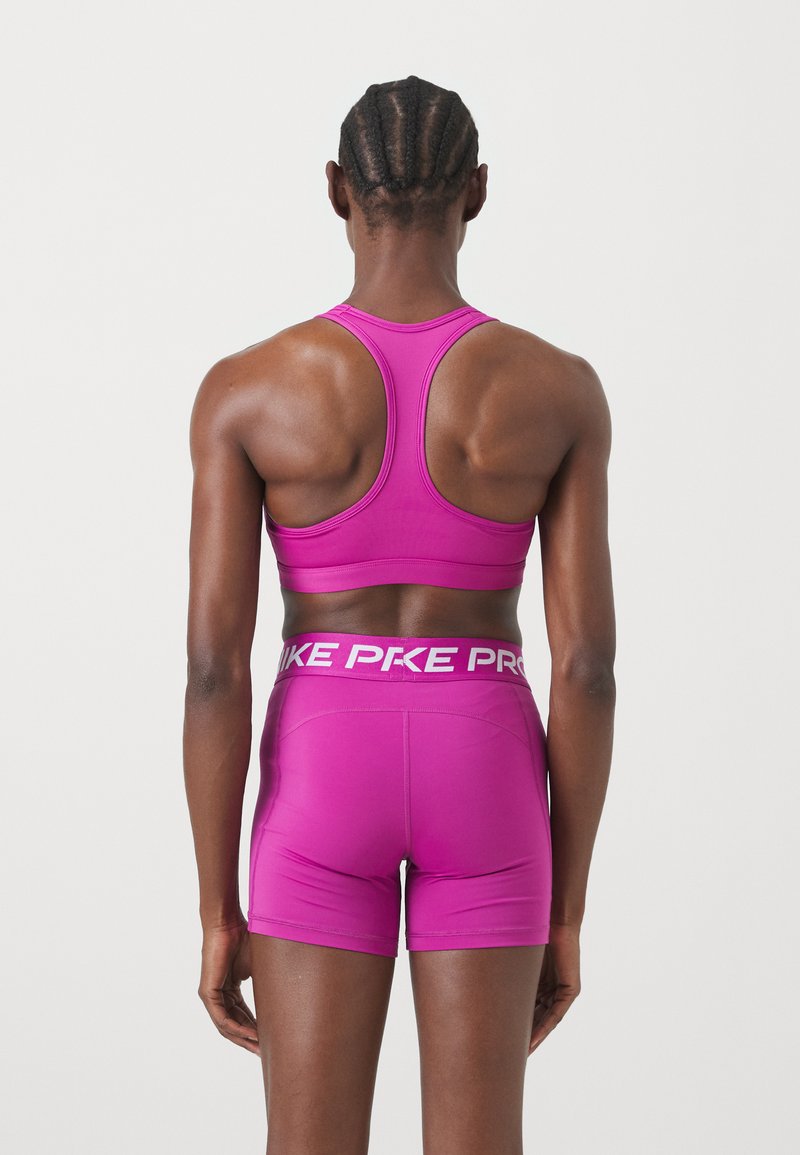 Figurbetontes pinkes Sportoberteil und Shorts mit Racerback-Design. Der Bund präsentiert das weiße "PKE"-Branding. Glatte Textur, minimale Nähte.