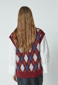 Burgundy ilman hihoja neulepaita, jossa on sinisten, harmaiden ja keltaisten timanttikuvioiden, sekä ribbaushelma. Siinä on v-kaula-aukko ja rento istuvuus.