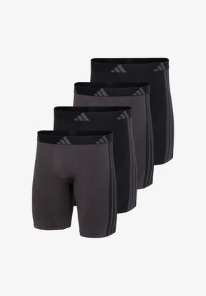 Athletischer junger Mann, barfuß stehend, ohne Hemd, trägt schwarze Kompressionsshorts bis zum Knie mit seitlichen Streifen und einem markierten Taillenbund.