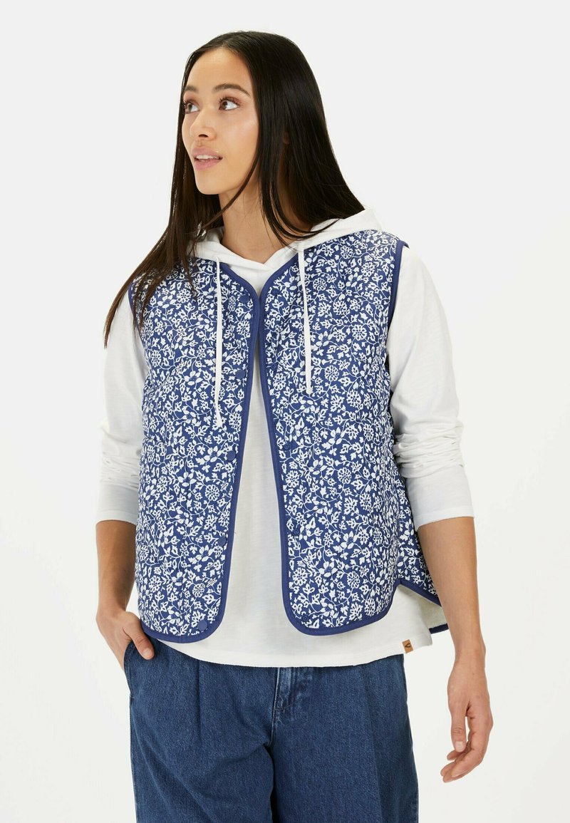 Blue floral-patterned vest with white accents, quilted texture, open front design, worn over a white hoodie and blue pants. Lightweight fabric.