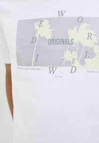 Hvid bomulds T-shirt med et grafisk print af palmer og tekst. Lysegrå og sorte accenter, enkel rund halsudskæring, afslappet pasform.