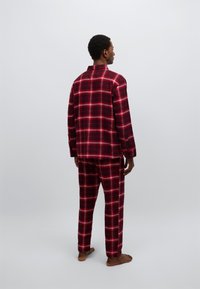 Κόκκινη και μαύρη καρό φανελένια πυτζάμα, με μακριά μανίκια και παντελόνια σε άνετη εφαρμογή, που παρουσιάζει καρό μοτίβο και απαλή υφή.