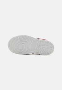 Hvid gummisål til sneakers med koncentriske cirkler og lineære mønstre, der har en rød øverste kant og tekstureret detaljering.