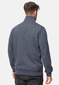 Marineblå zip-up sweatshirt med ribbet krave, manchetter og kant. Textureret stof med et subtilt meleret mønster. Bagfra.