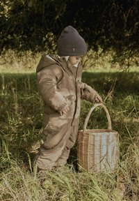 Pruun isolatsiooniga lumepüksid kapuutsiga, millel on elastsed varrukad, kanti halli kudumisega beanie'ga, hoides kudumisega korvi rohttaimede piirkonnas.