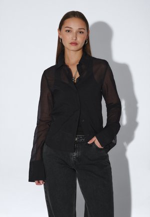 Sort, gennemsigtig skjorte med knapper, krave, lange ærmer og afslappet pasform. Bemærkelsesværdige detaljer inkluderer buet kant og unikke knaplukninger.