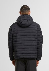 Chaqueta acolchada negra con capucha, patrón de tejido horizontal y dobladillo acanalado. Fabricada con un tejido ligero y texturizado con acabado mate.