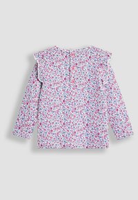 Langarmshirt mit weißem Hintergrund, verziert mit einem pinken und blauen Blumenmuster. Mit Rüschendetails und zwei pinken Knöpfen auf der Rückseite.