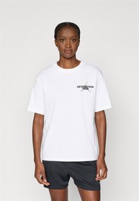 Balta medvilninė marškinė su trumpomis rankovėmis, puošti juodu „GENERATION HEIR“ tekstu su kryžminiais kardais. Dėvima su juodomis tinklinėmis šortais.