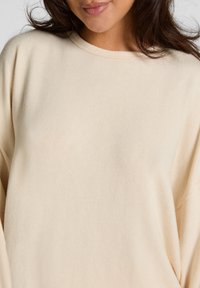 Lichtbeige sweatshirt met lange mouwen gemaakt van zachte stof. Beschikt over een ronde halslijn en een licht oversized pasvorm. Soepele textuur.