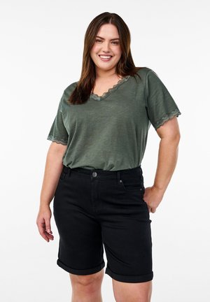 Camisa verde de manga corta con borde de encaje en el escote, combinada con pantalones cortos de mezclilla negros enrollados que cuentan con cierre de botón y bolsillos.