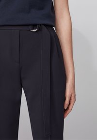 Námořnické kalhoty s hladkým, strukturovaným textilním materiálem; mají boční šňůrku a štíhlý střih. Viditelné kapsy a poutka na opasek zvyšují designové detaily.