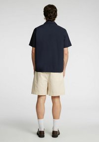 Námořnická košile s krátkým rukávem a límečkem, spárovaná se světlými šortkami. Tento outfit má volný střih a hladkou bavlněnou texturu.
