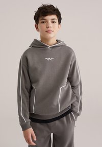 Hanorac gri cu glugă și detalii albe. Material moale, croială lejeră, logo frontal „SALTY”. Asortat cu pantaloni gri asortați.