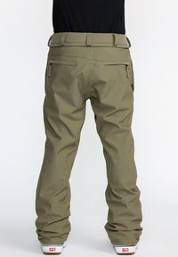 Pantalons de neige décontractés, verts olive, avec poches zippées, passants de ceinture et jambes légèrement amples, fabriqués dans un matériau résistant à l'eau.