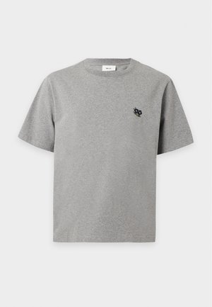 Mand stående iført en grå t-shirt med korte ærmer og logo, olivengrønne brede bukser og sorte sko mod en ensartet hvid baggrund.