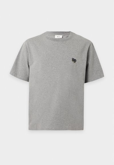 T-shirt gris à manches courtes et col rond avec une petite fleur noire et verte brodée sur le côté gauche de la poitrine.