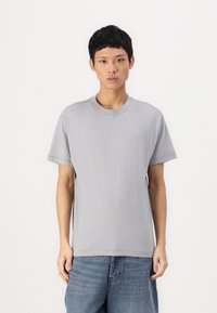 T-shirt in cotone grigio a girocollo con maniche corte, vestibilità rilassata e dettagli di cucitura sottili, abbinato a jeans in denim blu.