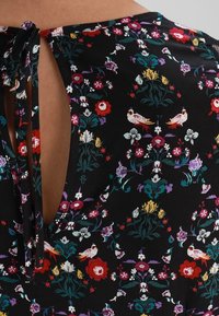 Tejido negro con coloridos patrones de flores y pájaros, que presenta un escote en forma de llave atado con cuerdas de tela a juego.
