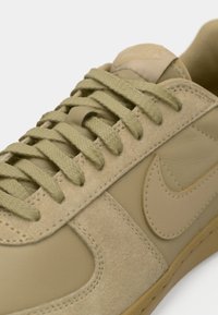 Beige sneakers met een glad leren bovenwerk en suede accenten, ronde veters en een rubberen zool. Aan de zijkant staat een subtiele logodetail.