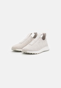 Baskets de sport beige clair avec un dessus en tricot texturé, des bandes élastiques et une semelle en caoutchouc blanche. Présente des accents de logo sur les bandes.
