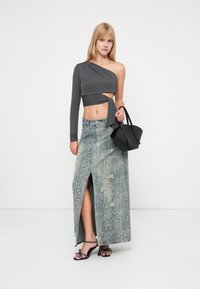 Sivý crop top s jedným ramenom v kombinácii s denims skritom s hadím vzorom a vysokým rozparkom, čiernou kabelkou; zlaté akcenty a čierne sandále na opätku.