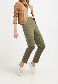 Tan suède cropped jack, witte top, olijfgroene broek met hoge taille, witte sneakers, met een ontspannen pasvorm en omgeslagen zomen.