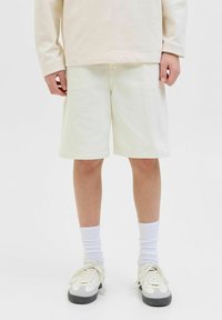 Pantalones cortos de algodón blancos con un ajuste relajado, que presentan costuras planas y bolsillos laterales, combinados con calcetines blancos y zapatillas con acentos grises.