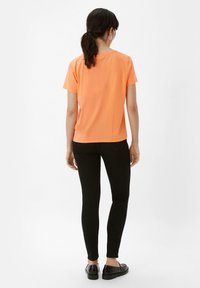 Kurze Ärmel, orange Baumwoll-T-Shirt, kombiniert mit schwarzen schmalen Jeans und schwarzen Slippern. Einfaches Design mit einer lockeren Passform.