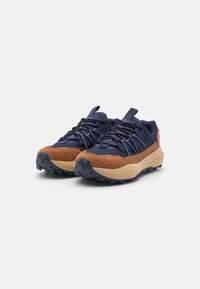 Blaue und braune Sportschuhe mit einem strukturierten Wildleder-Obermaterial, Gummisohlen und einem komplexen Schnürsystem. Auffälliges, robustes Profil für eine verbesserte Traktion.