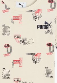 Béžové tričko s rôznymi potlačenými grafikami, vrátane bežeckých postáv, čísla 9.58 a loga PUMA s čiernymi a červenými akcentmi.